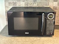 Front view of RCA black microwave showing the glass door, model branding, handle, and control panel with digital display showing 'End'.