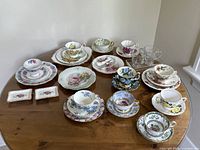 Wide view of entire lot showing multiple floral china tea cups, saucers, plates and rectangular dishes on wooden table.