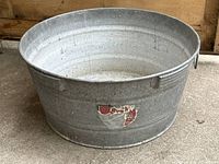 Large round galvanized steel wash bucket with visible age wear and label remnants.