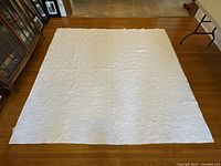 Full view of the white cotton quilt spread out on a wooden floor showing its size and overall design.