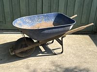 Side view of the blue metal wheelbarrow showing rust on metal tub and wooden handles.