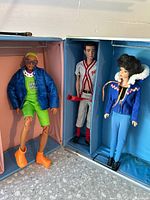 Three dolls displayed upright in divided compartments of the open blue metal case