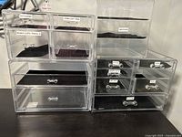 Four clear acrylic drawer sets stacked on a dark surface, multilingual labels on drawers visible.