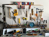 Wide view of pegboard with hand tools hanging including hammers, screwdrivers, scissors, levels, and trays with miscellaneous tools below