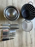 Knives, bowls, colander and metal strainers laid out on the floor to show all items included.