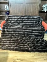 Photo of entire faux fur blanket spread across an orange sofa, showing the striped black and grey furry side.