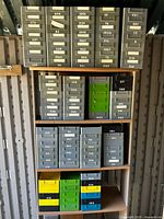 Front view of multiple shelving racks holding the grey plastic bins with white removable labels and a few colored bins at the bottom shelf.