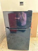 Front view of the compact Hisense small refrigerator with freezer compartment. Black finish with visible wear marks.