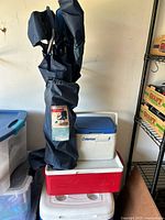 Three ice chests stacked, folding camp chair in carrying bag leaning on them