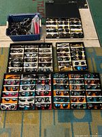 Six trays of assorted sunglass frames and lenses arranged on floor with a blue basket of loose frames