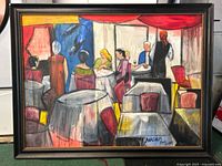 Framed oil painting showing an indoor scene with individuals at tables, in an abstract style with bright colors.
