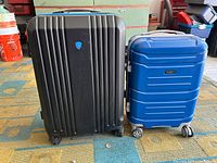 Overview of both brownish gray large and blue medium hard shell suitcases side by side on floor