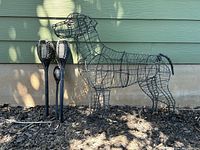 Wire dog sculpture shown beside three outdoor solar torch lights placed in ground with mulch background and green siding