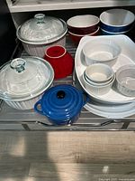 Full set of Pyrex ceramic cookware including casseroles with clear glass lids, colorful bowls, ramekins, and a blue pot.