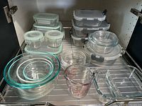 Overview of all glass containers and measuring cup arranged on a rack inside a cabinet