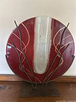 Front view of large circular red glass vase with white center and gold accents on metal stand with branch-like supports.