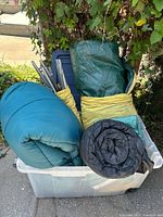 Plastic storage bin filled with three sleeping bags and tent bags.