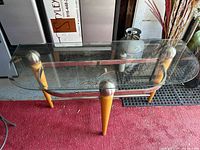 Top-down angled view showing the clear glass top, wood legs, metal spherical accents, and lower metal support rod.