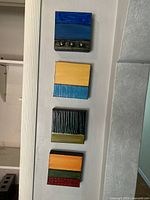 Four 6x6 inch square oil paintings arranged vertically on a wall, each with a different abstract design.
