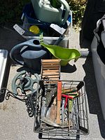 Top-down view of assorted garden items including watering cans, hand tools, metal basket, and plastic storage container.