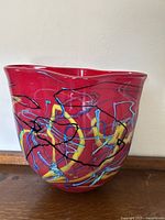 Front view of the red glass vessel showing vibrant abstract swirl pattern