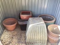 Wide shot of various large garden pots arranged inside a metal shed corner, showing different shapes and materials
