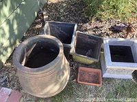 Various garden pots in round, square, and rectangular shapes including terracotta, stone, and concrete materials shown outside on soil with dirt and debris