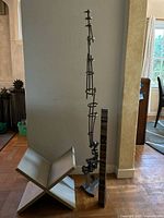 Full view of the tall metal sculpture and wooden X-shaped magazine rack side by side in room corner.