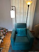 Photo of teal swivel armchair with matching cushion and two different floor lamps in living room setting.