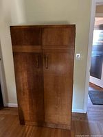 Full front view of the vintage dark brown wood armoire with two doors and vertical handles.