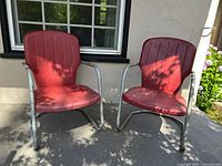 Pair of vintage red metal patio chairs on patio with silver tubular frames and contoured seats and backs.