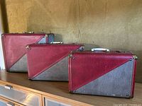 Photo showing three sizes of red and gray hard shell suitcases with white handles and brass corner protectors.