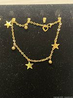 Photo showing the gold filled star charm bracelet laid out flat on a black surface, displaying the star and bead charms and heart-shaped loop near the clasp.