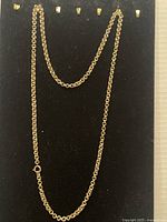 Long gold filled linked chain necklace shown fully extended against a black background to display length and detail of links.