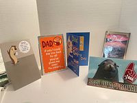 Five different Father's Day cards standing upright, showing front designs including a squirrel with a pun, an orange-faced cartoon with text, a mountain scene, and a seal image with 'Seal of Approval'.