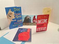 Five assorted Father's Day cards displayed, showing front designs including dog illustration, seal with 'Seal of Approval,' red card with bold white and yellow text, yellow embossed card, and blue foam '#1 Dad' hand card.