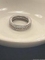 Sterling silver ring with two rows of clear stones placed on a white dish for clear view of stones and band details.