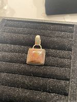 Close-up of the sterling silver charm with the square gemstone on a black textured surface.