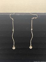 Pair of .925 sterling silver dangle earrings displayed on black velvet, showing their thin, curved bar and spherical bead design.
