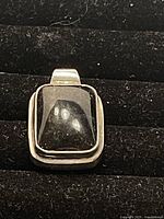 Front angle view of the sterling silver pendant with a dark rectangular gem on black background.