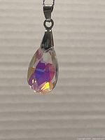 Close-up of Swarovski crystal teardrop pendant with faceted surfaces reflecting multicolor light, hanging from a silver bail and chain.