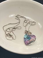 Full view of the silver chain and heart-shaped Swarovski crystal pendant resting in a white dish.