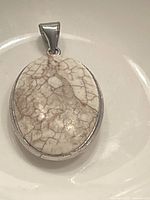 Oval pendant with cracked white and brown stone set in silver, front view showing stone and bail.