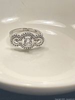 Close-up photo of the silver ring resting on a white surface showing detailed beaded work and central snowflake-like crystal.