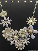 Full view of necklace showing multiple flower motifs made with pastel stones and crystals on gold-tone chain.