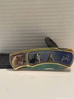 Side view of folding pocket knife showing wolf artwork and Al Agnew signature on handle, with black textured sleeve case behind.