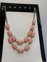 Front view of gold tone double chain necklace with pink rectangular and oval stones on black display board.