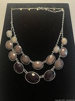 Full view of the necklace laid flat on a black background showing the faceted large oval stones and silver-tone chain.