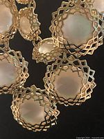 Close-up photo showing the detailed lattice filigrana circular settings with translucent or white inset stones on the necklace chain.