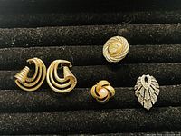 Four pairs of mismatched earrings arranged on black velvet surface, showing different shapes and materials.